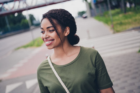 Charming young woman enjoying a sunny walk in the city with a joyful smile, embodying a modern and stylish urban lifestyle.の写真素材