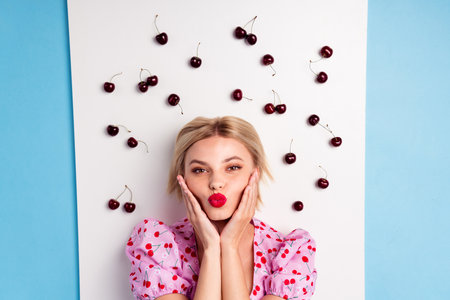 Playful young woman posing with cherries, wearing a cheerful cherry printed outfit, showcasing a summery and stylish moodの写真素材