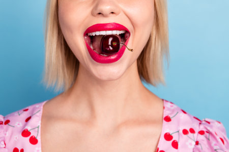 Close up photo of cheerful cute lovely girl wear stylish pink print clothes enjoy sweet cherries isolated on blue color backgroundの写真素材