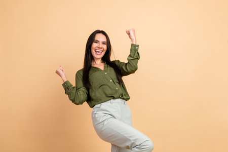 Joyful woman celebrating success against a beige background, radiating positivity with a cheerful smile and expressive victory pose.の写真素材