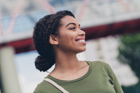 Charming young woman smiling outdoors in urban setting on a sunny day, radiating happiness and confidence in casual styleの写真素材