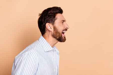 Side profile of a young stylish man in a striped shirt with a joyful expression against a beige backgroundの写真素材