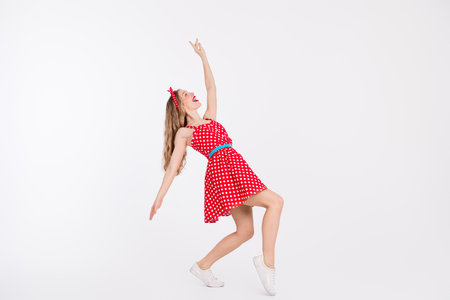 Young woman in vintage red polka dot dress dancing joyfully on white backgroundの写真素材