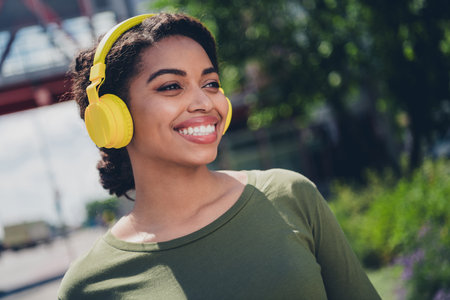 Young woman in a casual t-shirt enjoys music with yellow headphones while walking outdoors during a...