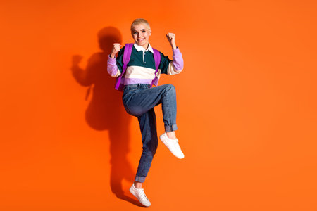 Joyful young female student posing on an orange background in casual fashion style, showcasing a...