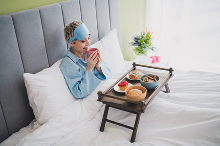Woman Enjoying a Cozy Morning in Bed Sipping a Warm Drink with Breakfastの写真素材