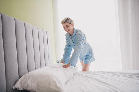 Young Woman in Blue Pajamas Making Bed at Home in Brightly Lit Bedroom