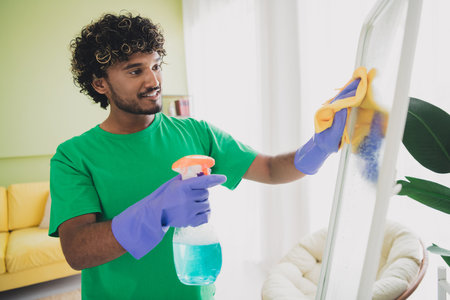 Portrait of nice young man clean wipe mirror glass wear t-shirt modern green interior flat indoorsの写真素材