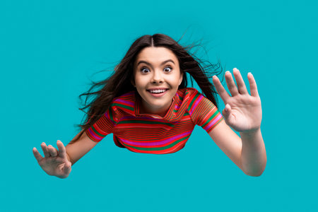 Excited young brunette against turquoise background, playfully reaching out wearing vibrant striped...