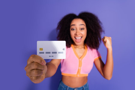 Excited Young Woman Holding a Bank Card While Celebrating Against a Purple Background, Promoting Shopping and Financial Transactionsの写真素材