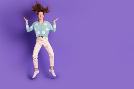 Young cheerful female in casual style jumps against a vibrant purple background, showcasing happinessの写真素材