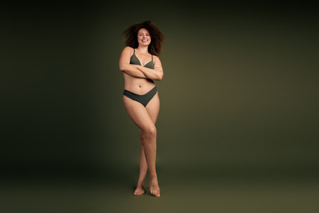 Confident young woman posing in lingerie on a solid background, embracing natural beauty and body positivityの写真素材