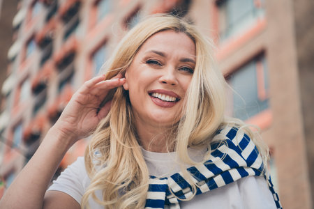 Charming blond woman smiling outdoors in casual style enjoying a sunny day in the cityの写真素材
