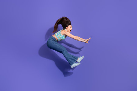 Young cheerful woman in stylish casual outfit jumping joyfully against a vibrant purple background