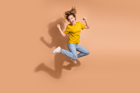 Cheerful young woman in casual style jumping joyfully on a vibrant beige background inspiring...