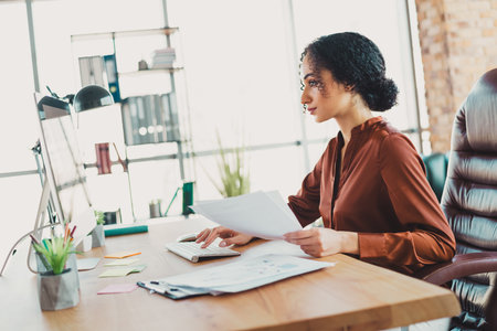 Focused businesswoman working at her desk in a modern office with natural lighting and organized workspace for productivityの写真素材