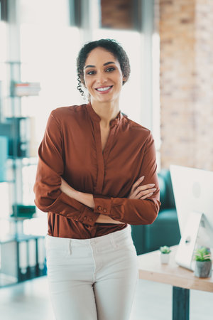 Confident businesswoman standing in modern office, smiling as she poses, showcasing professional demeanor and casual work attireの写真素材