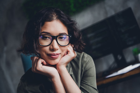 Portrait of a confident female programmer in casual attire, sitting at her workspace with a...