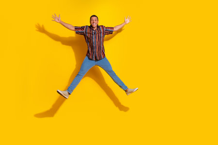 Energetic young man jumping with excitement against a vibrant yellow background showcasing stylish...