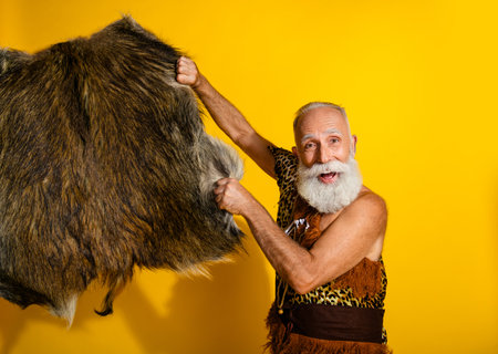 Portrait of aged primeval caveman hold animal skin leather isolated on yellow color backgroundの写真素材