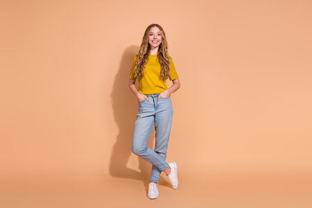 Stylish young woman in a casual outfit showcasing confidence on a solid beige backdropの写真素材