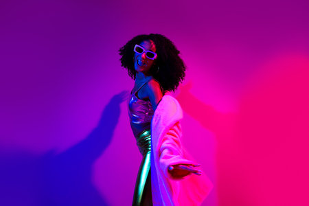 Glamorous young woman posing under vibrant neon lights in an energetic nightclub atmosphereの写真素材