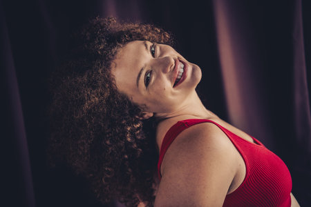 Beautiful young woman in vibrant red outfit, smiling confidently against a soft purple background