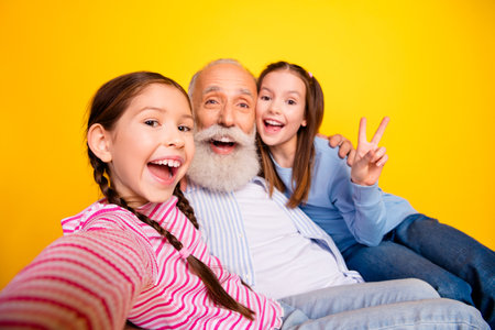 Joyful elderly man with two young girls enjoying a bright yellow background together