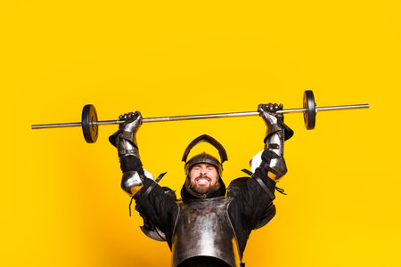 Knight in antique armor lifting a weight with a vibrant yellow backgroundの写真素材