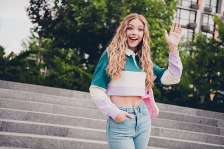 Portrait of pretty young girl rucksack arm wave hi you wear top city center outdoorsの写真素材