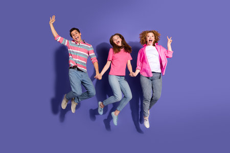 Three young friends jumping with joy against a vibrant purple background, showcasing youthful...
