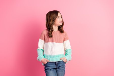 Happy young girl with wavy brown hair in a colorful sweater against a vibrant pink background, radiating charm and happinessの写真素材