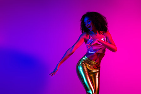 Stylish young woman dancing under vibrant neon lights in a retro-inspired environment showcasing captivating colorsの写真素材