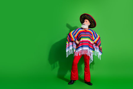 Cheerful elderly man in colorful traditional Mexican attire posing confidently against a vibrant green backgroundの写真素材