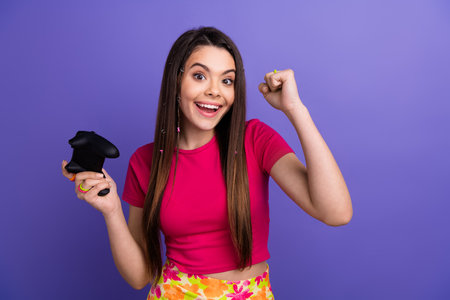 Smiling young woman holding game controller and celebrating victory on a purple background