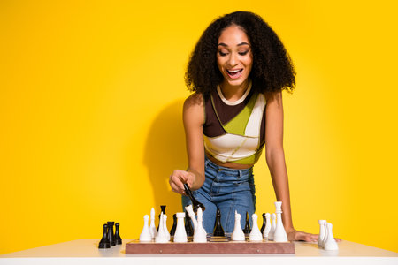 Stylish young woman playing chess with a bright yellow background in a cheerful setting