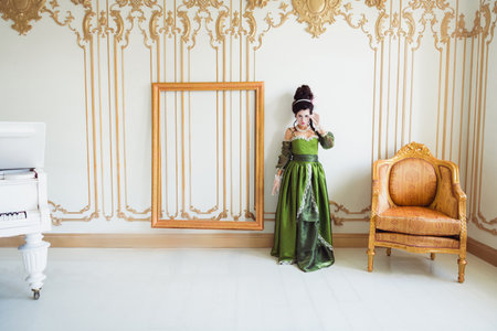 Elegant woman in green historical renaissance costume in a luxurious interior with a gold frame and...