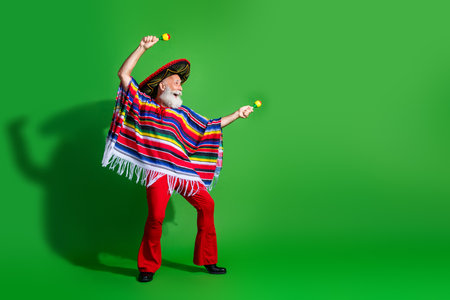 Cheerful elderly man in vibrant traditional Mexican attire celebrating with maracas against a bright green backdropの写真素材