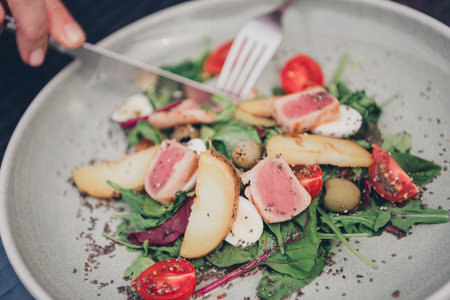 Fresh and colorful salad with seared tuna slices, avocado, and cherry tomatoes on a rustic plateの写真素材