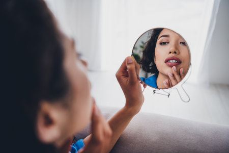 Young woman exploring her reflection in a mirror while relaxing at home on a calm day enjoying a serene and domestic atmosphere indoorsの写真素材