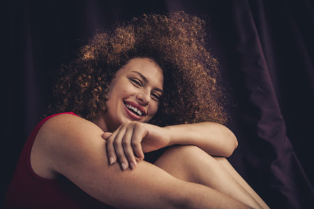 Portrait of a Confident Young Woman with Natural Curly Hair Smiling Joyfully Against a Studio Settingの写真素材