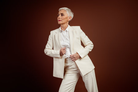 Elegant Senior Fashion Model in a Stylish White Suit Against a Brown Background Representing Confidence and Professionalismの写真素材