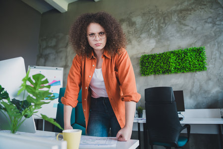 Successful young businesswoman working in modern office, standing confidently at work desk with...