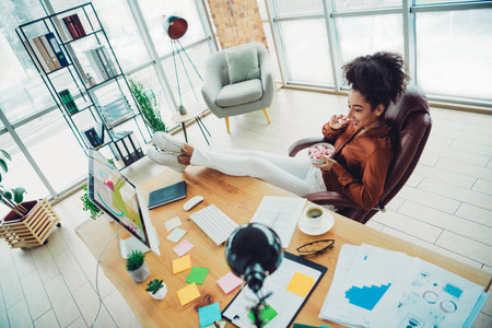 Casual young businesswoman enjoying a relaxed break at her desk in a bright modern office with stylish interior designの写真素材