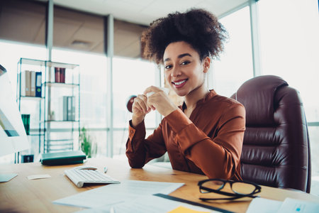Young businesswoman smiling confidently at her office desk amidst a modern interior loft workspace...