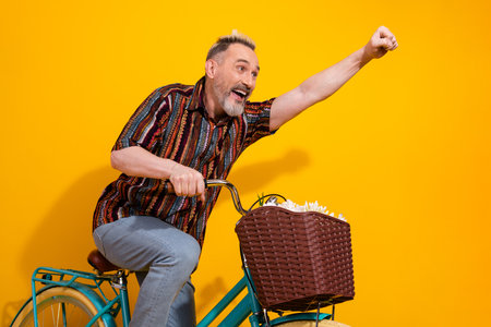 Energetic middle aged man in vibrant outfit riding a bicycle and striking a fun pose indoors against...
