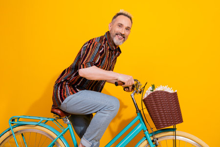 Cheerful middle aged man riding a trendy vintage bicycle in a yellow studio background with a joyful expression and stylish outfitの写真素材