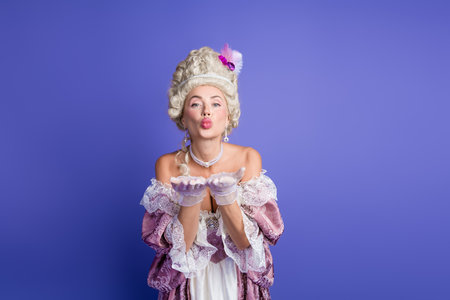 Elegant woman in baroque court attire blowing a kiss against a vibrant purple backgroundの写真素材