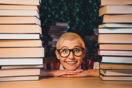 Young woman with short blonde hair and glasses surrounded by books, smiling widely in a cozy home library settingの写真素材
