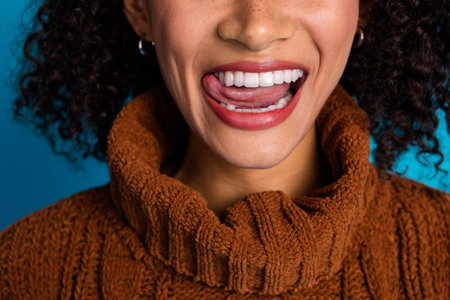 Attractive young woman in a brown knitted sweater with a vibrant blue background expressing joy